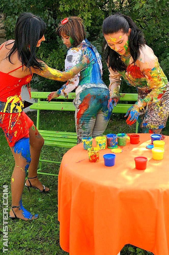 Clothed women cover themselves in finger paint on a garden bench