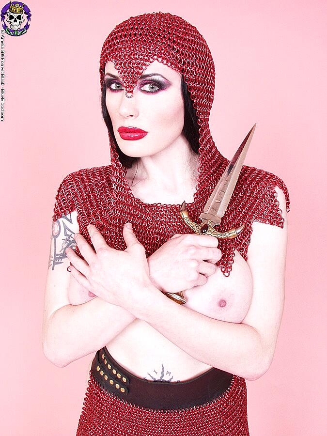 Busty chick Morrigan Hel licks a dagger while wearing chain mail and OTK boots